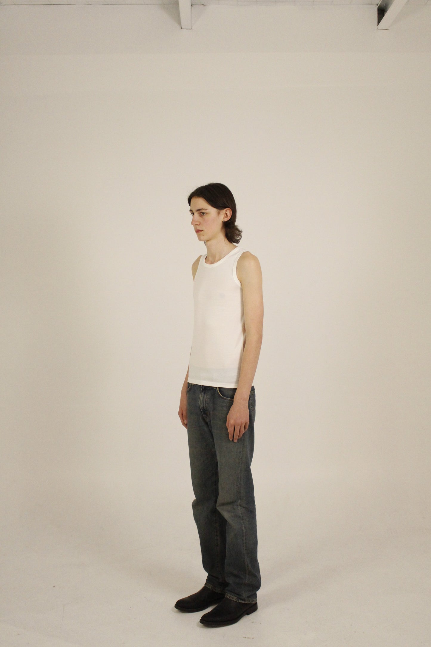 White minimalist ribbed tank top worn in a relaxed standing pose. The model is angled and the pose highlights clean lines and everyday wearability