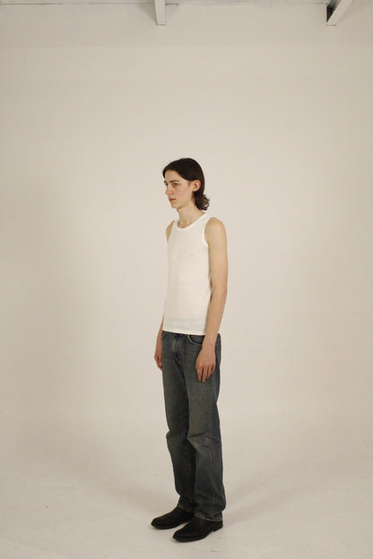 White minimalist ribbed tank top worn in a relaxed standing pose. The model is angled and the pose highlights clean lines and everyday wearability