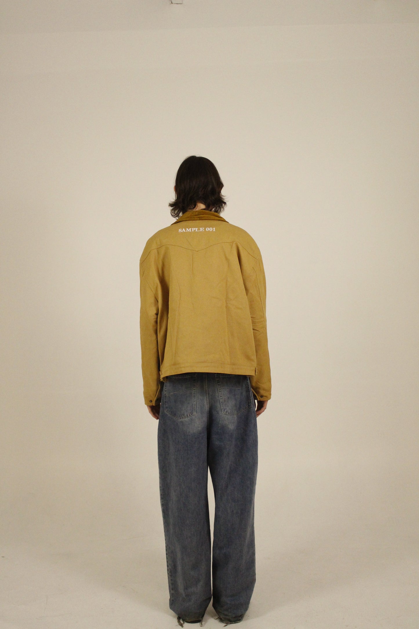 Back view of model wearing SAMPLE_001 canvas utility jacket with embroidered Vision Studios logo, showing cropped workwear fit and structured silhouette