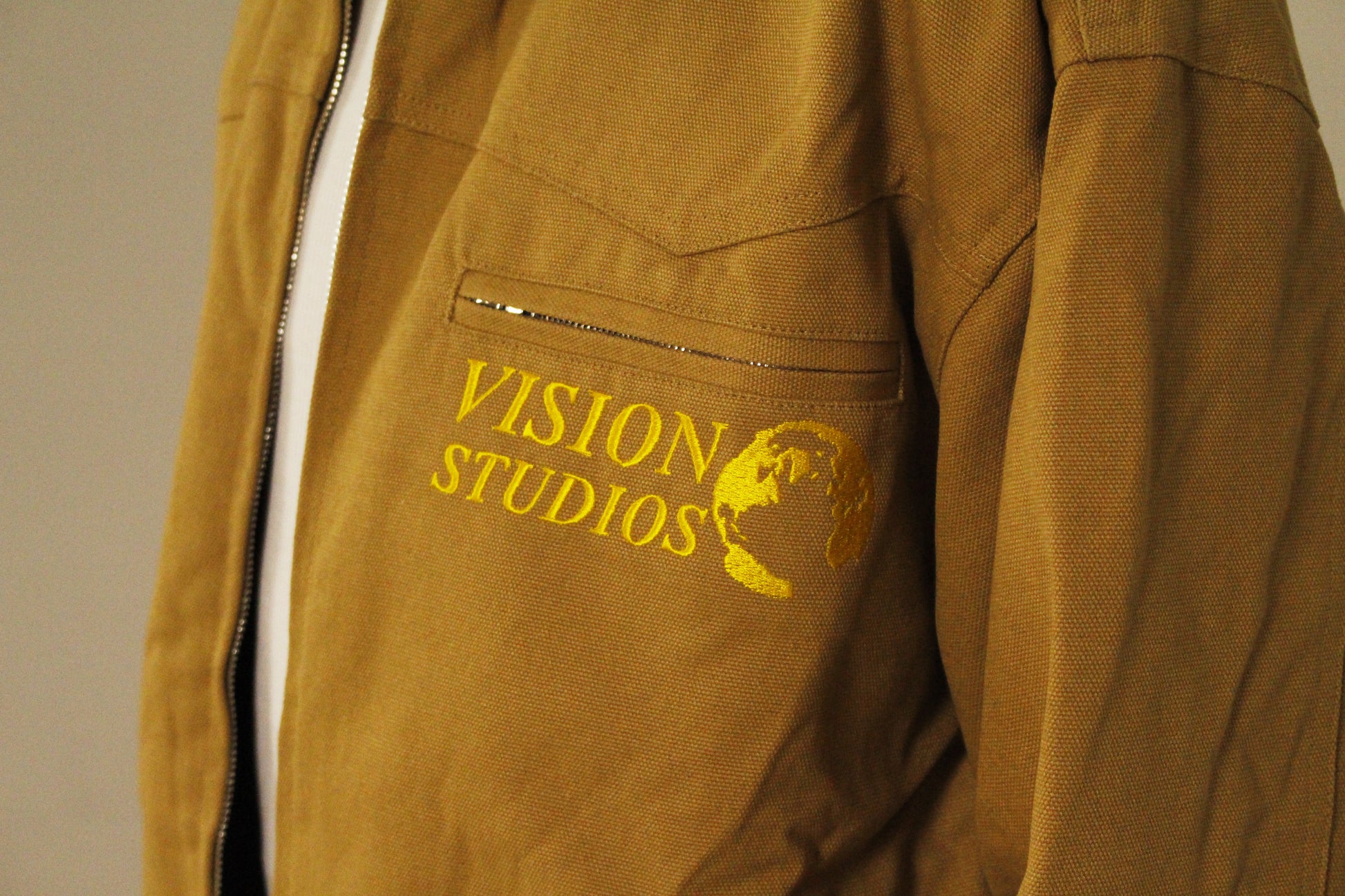 Close-up of SAMPLE_001 canvas utility jacket showing Vision Studios embroidered logo detail and front chest pocket