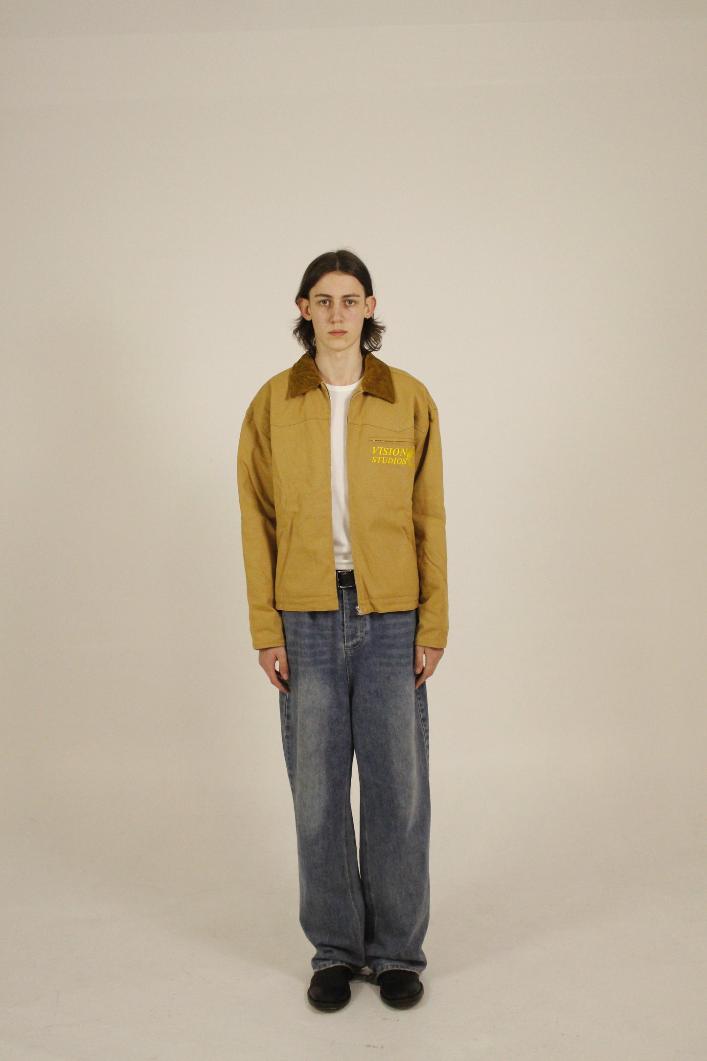 front view of model wearing SAMPLE_001 canvas utility jacket unzipped with embroidered Vision Studios logo, showing cropped workwear fit and structured silhouette