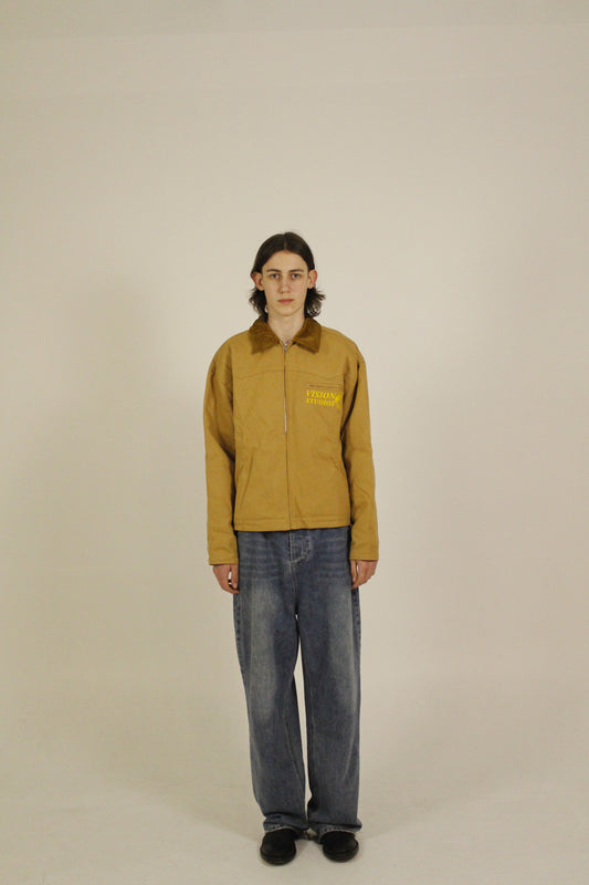Side view of model wearing SAMPLE_001 canvas utility jacket zipped with embroidered Vision Studios logo, showing cropped workwear fit and structured silhouette
