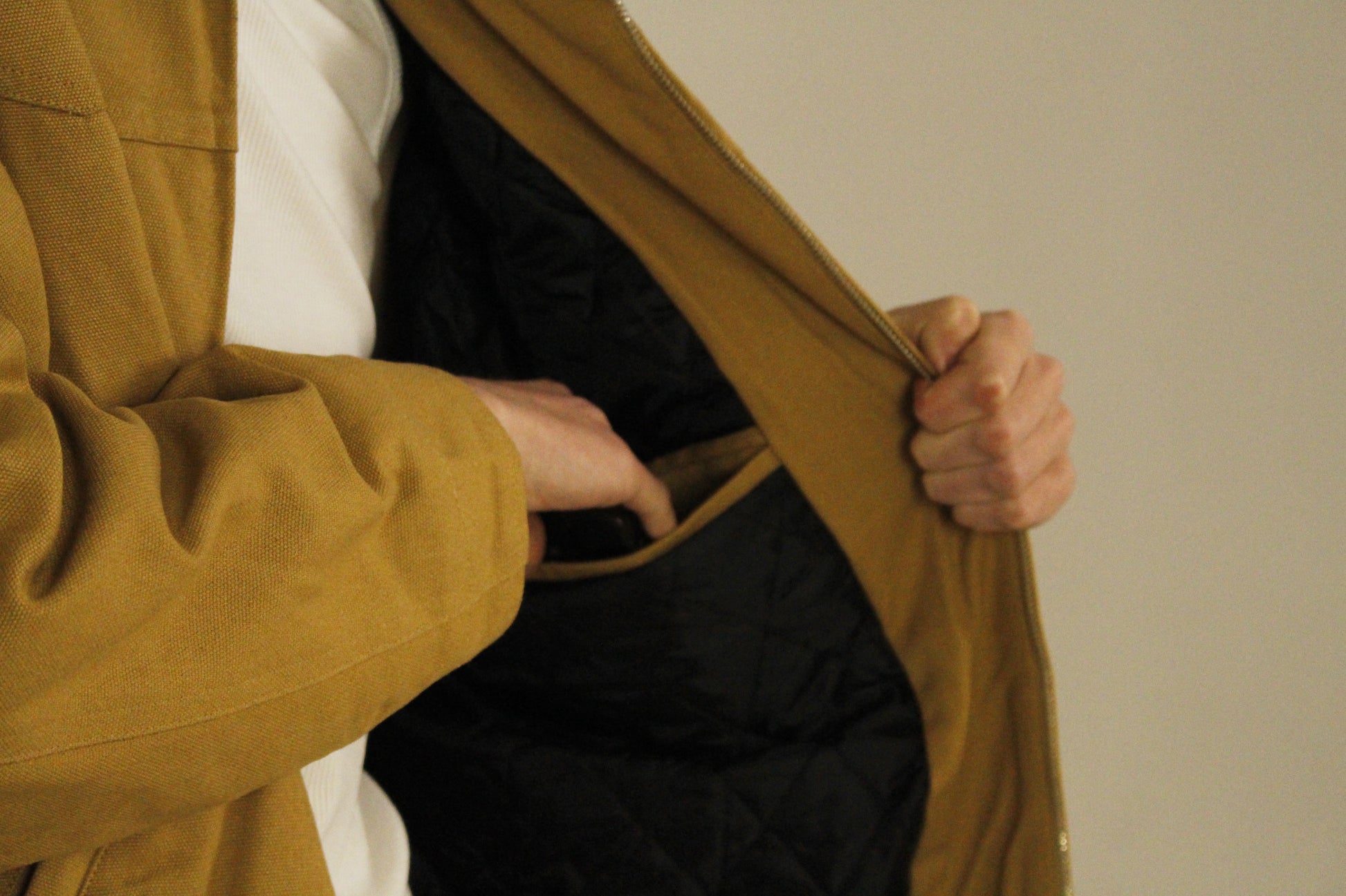 Close-up of SAMPLE_001 canvas utility jacket showing a hand placing an item in the inner pocket of the jacket