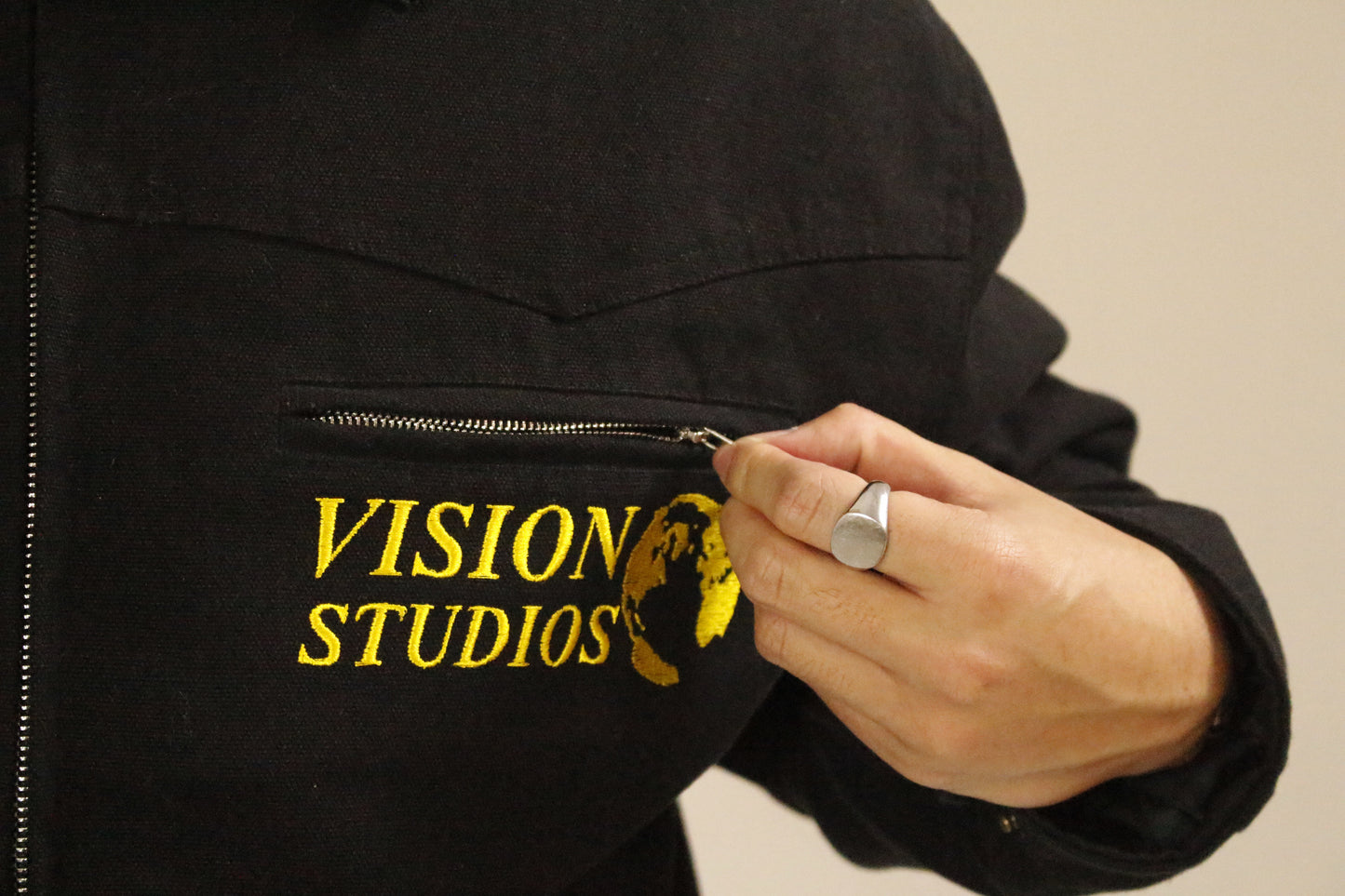 Close-up of SAMPLE_001 canvas utility jacket showing Vision Studios embroidered logo detail and front chest pocket