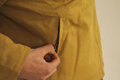 Close-up of SAMPLE_001 canvas utility jacket showing a hand zipping the side pocket of the jacket