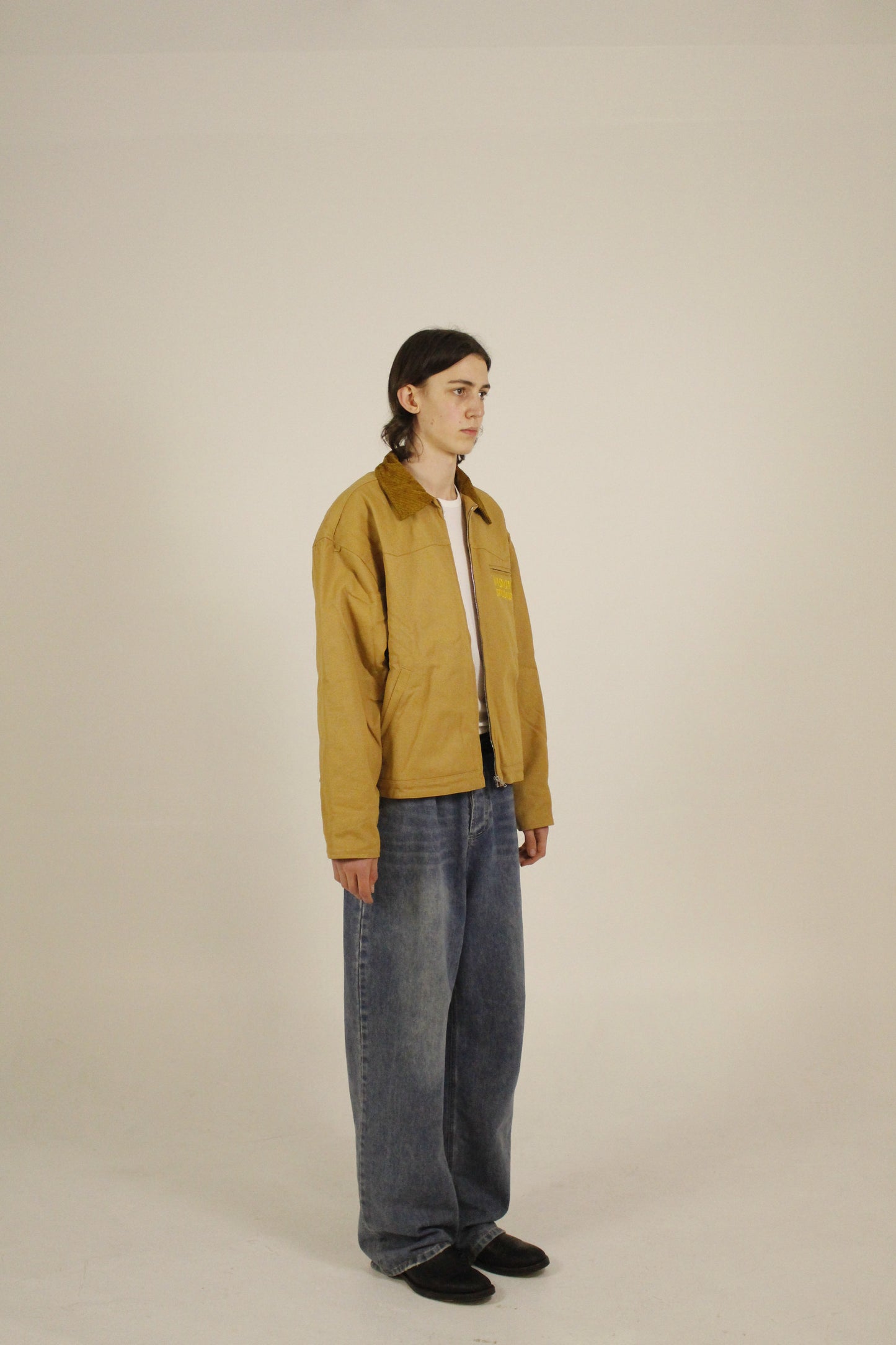 Side view of model wearing SAMPLE_001 canvas utility jacket unzipped with embroidered Vision Studios logo, showing cropped workwear fit and structured silhouette