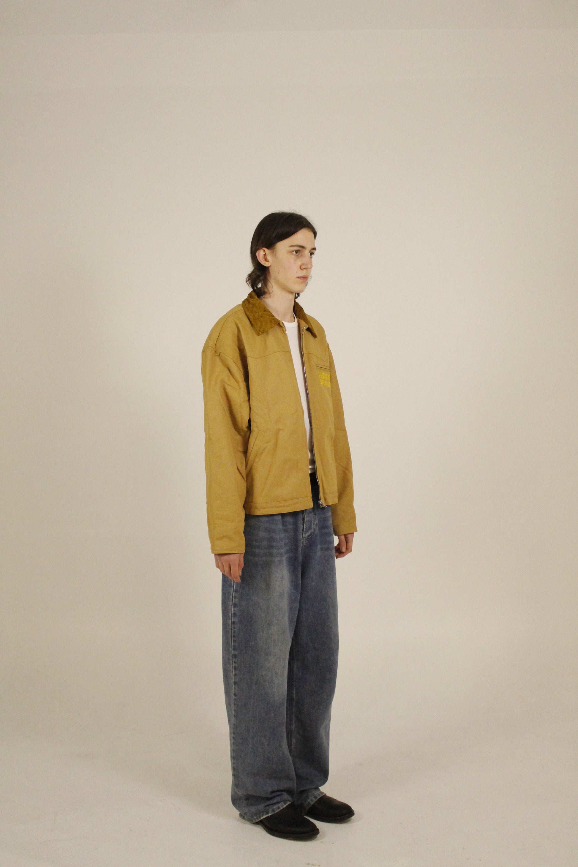 Side view of model wearing SAMPLE_001 canvas utility jacket unzipped with embroidered Vision Studios logo, showing cropped workwear fit and structured silhouette