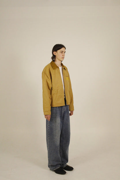 Side view of model wearing SAMPLE_001 canvas utility jacket unzipped with embroidered Vision Studios logo, showing cropped workwear fit and structured silhouette