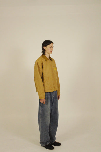 Side view of model wearing SAMPLE_001 canvas utility jacket zipped with embroidered Vision Studios logo, showing cropped workwear fit and structured silhouette
