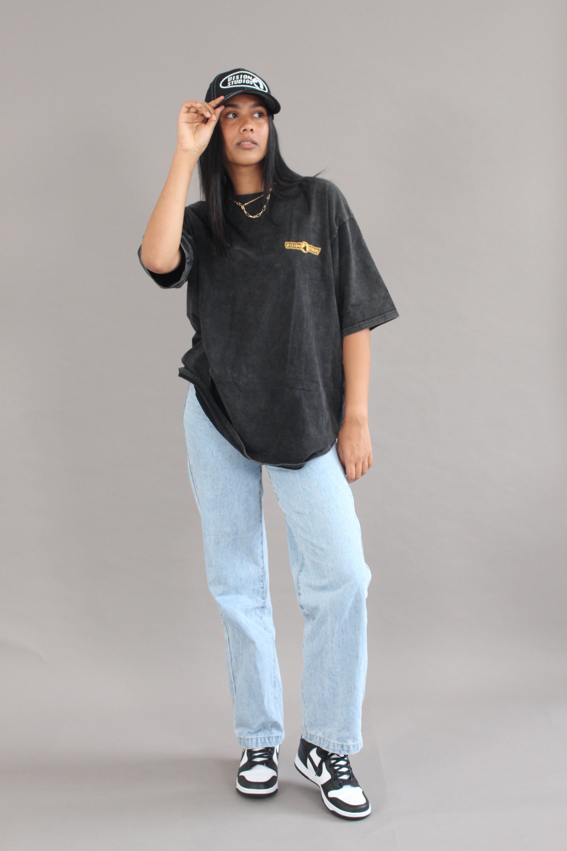 A model wearing a casual outfit posing with the black vision studios trucker hat and acid black vision studios oversized tee